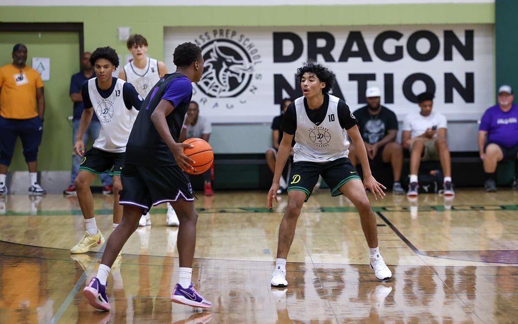 Two basketball players in action on a gym court with a "DRAGON NATION" sign in the background.