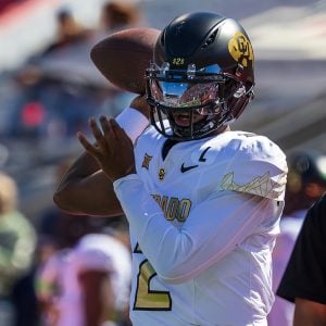 A football player in a white and gold uniform prepares to throw a football.