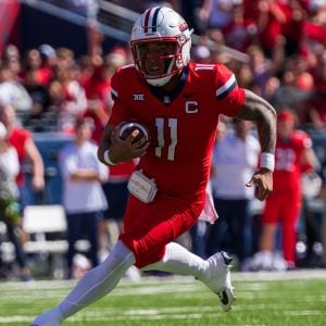 Football player in red uniform running with the ball on the field.