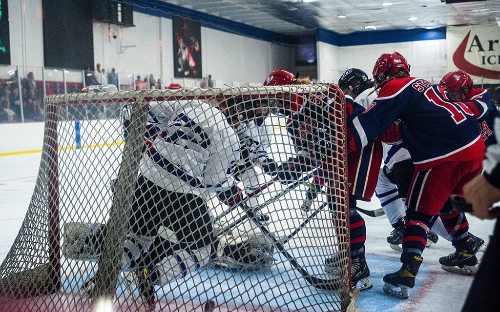 Arizona Wildcats women's ice hockey players in red and blue uniforms compete near the goal in an indoor rink.