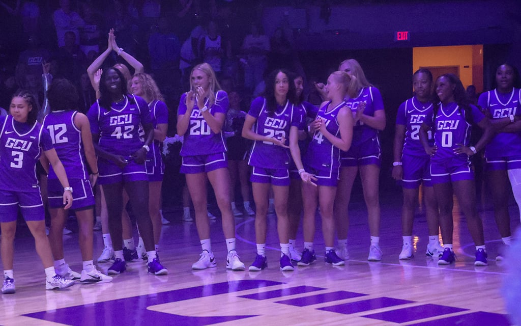 GCU female basketball players in purple uniforms standing on a dimly-lit court.