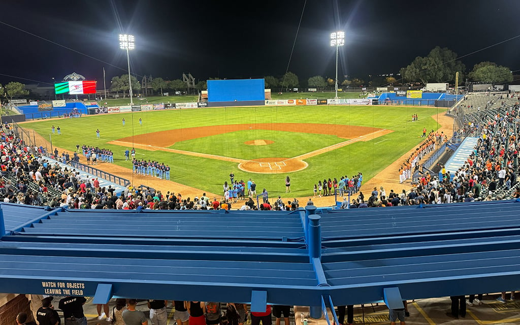 Nighttime baseball game with players lined up on the field and full stands.