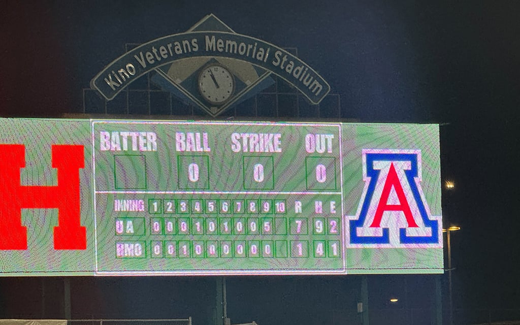 Scoreboard at Kino Veterans Memorial Stadium displaying inning scores for teams "UA" and "ENQ" with a clock logo above.