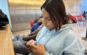 Jaqueline Lopez (blue hoodie) sits in the air-conditioned respite center at the Burton Barr Central Library as she scrolls through her phone. (Photo by Jalen Woody/Cronkite News)