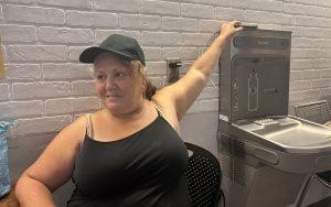 Monica Peña (black top) sits in the respite center away from the blazing hot temperatures in downtown Phoenix as she charges her phone. (Photo by Jalen Woody/Cronkite News)