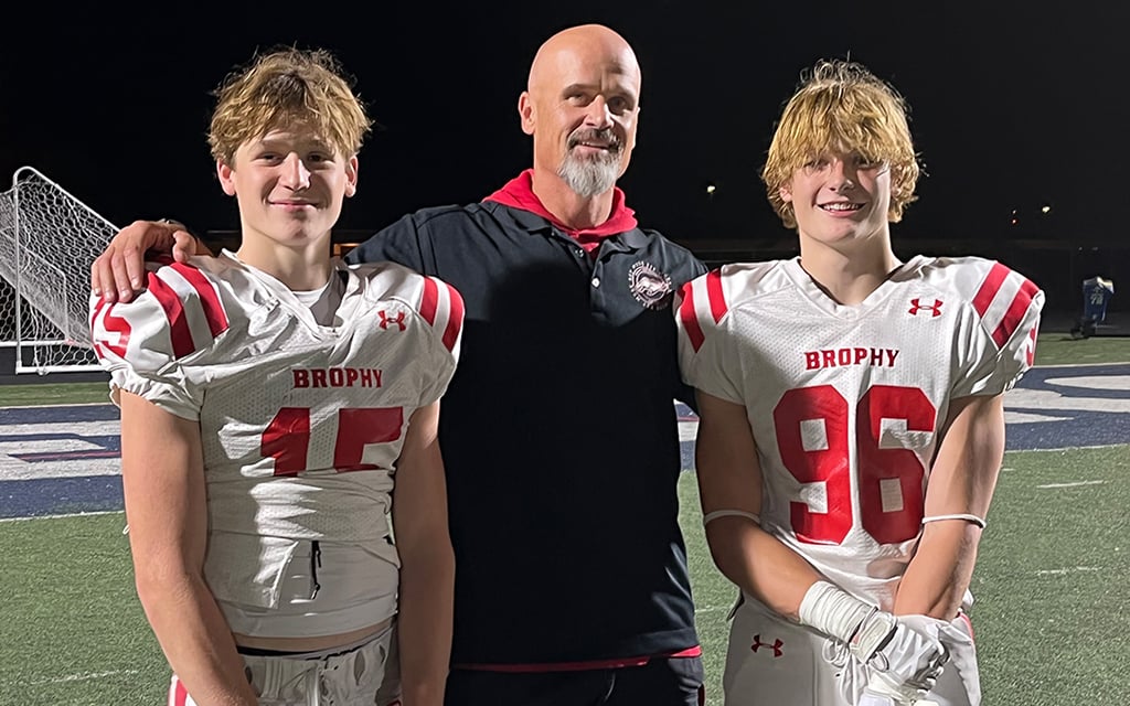 Case and Bastian Vanden Bosch, in white uniforms, and Kyle Vanden Bosch in a black jacket standing on a sports field at night.