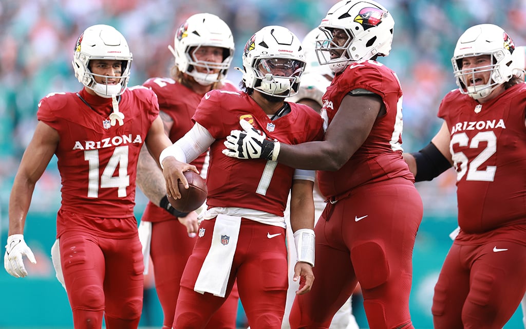 Arizona Cardinals quaterback Kyler Murray in a red uniform, with one arm holding a football.