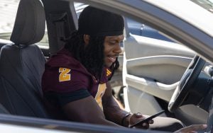 Arizona State running Back Kyson Brown holding his phone in a new car.