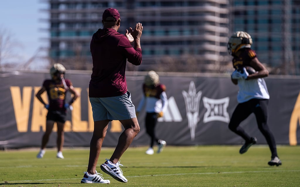 Hines Ward cheering on ASU football players during practice with buildings in the background.