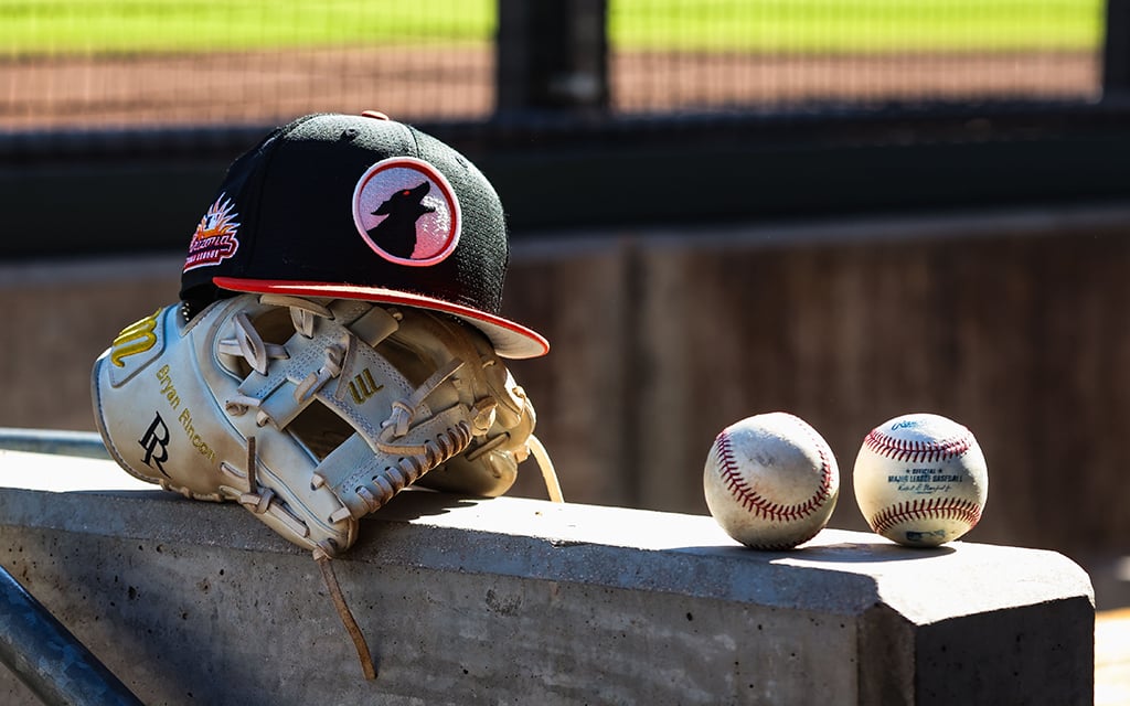 Baseball glove, Glendale Desert Dogs cap, and two baseballs on a concrete surface.