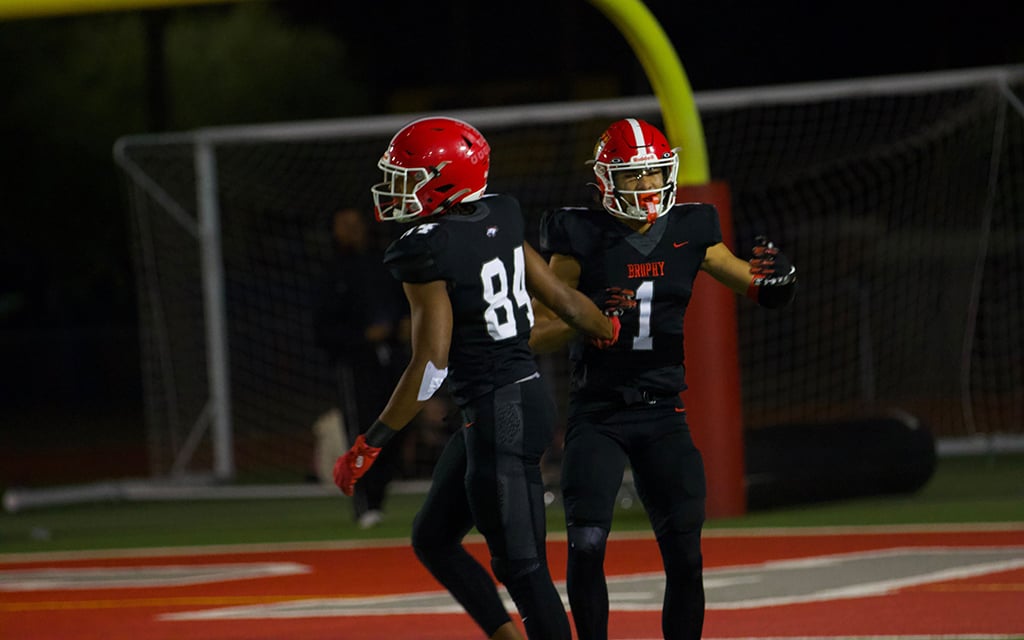 Brophy Prep wide receivers Devin Fitzgerald and Daylen Sharper in the black uniforms and red helmets celebrating on a field at night.