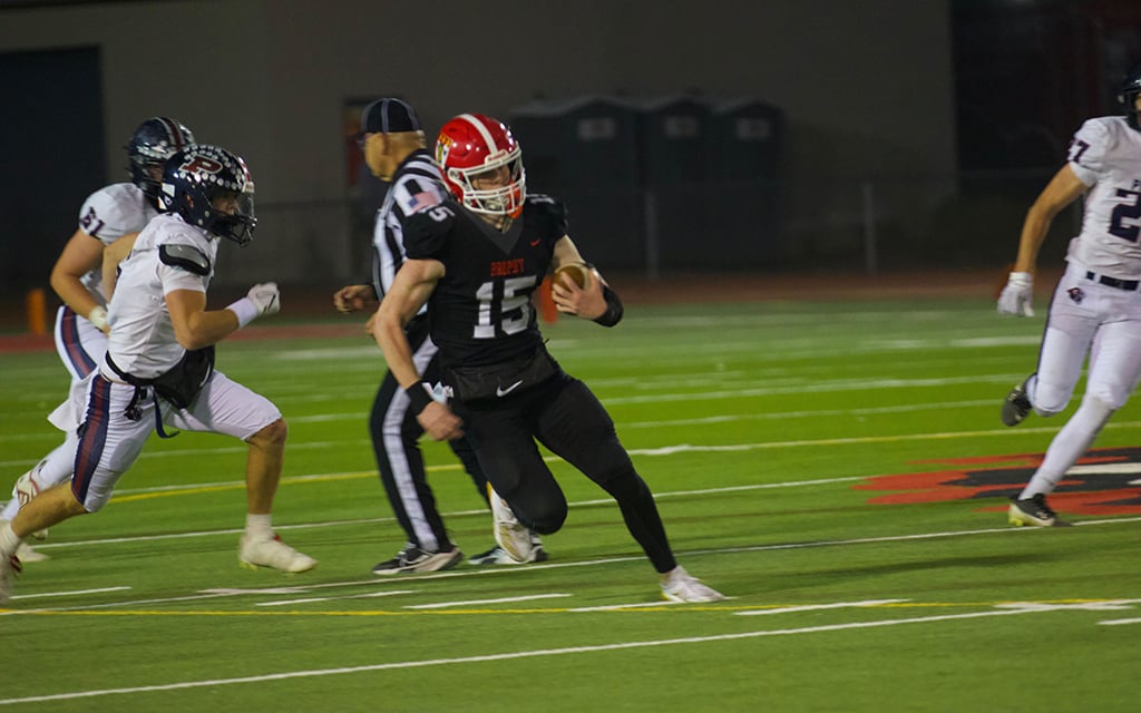 Brophy quarterback Case Vanden Bosch in the black uniform running with the ball while being chased by a player in a white uniform.