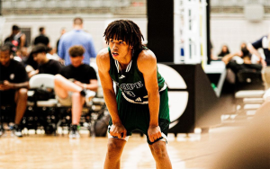 Basketball player in green and white jersey slouches over with his hands on his knees